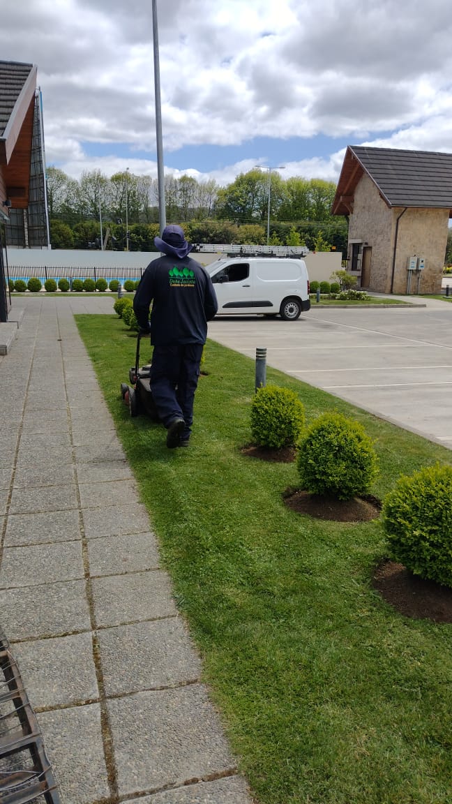 Jardinero con uniforme institucional cortando césped junto a sendero y furgón de servicio